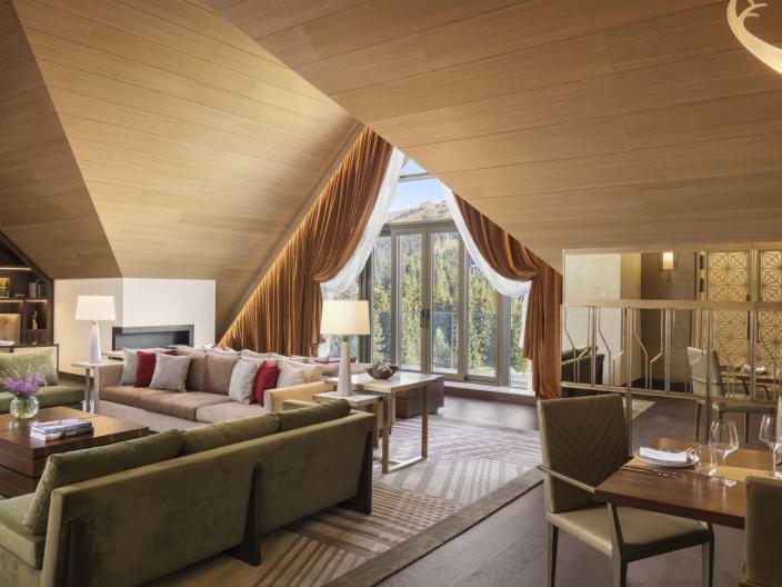 The living space of a penthouse suiter with 2 couches, a large dining table, a floor to ceiling bookshelf and unique drop ceilings A washroom with a large double sink vanity and a soaker tub in a penthouse suite at Viceroy Kopaonik Serbia