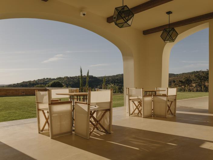 A sunny arched courtyard at Viceroy Ombria Algarve, featuring two tables surrounded by wood chairs, in view of the Algarve countryside