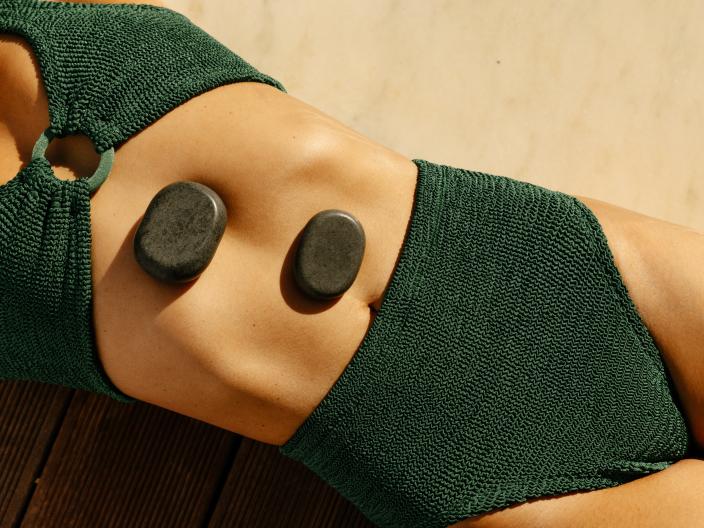A woman in a green swimsuit lies with stones on her torso