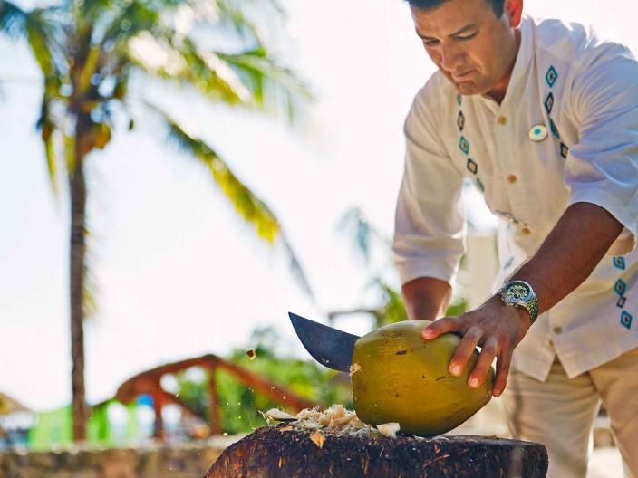 A man slicing a coconut with a machete