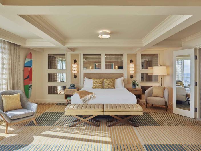 A King Bed in a large suite, with an arm chair and a surfboard mounted on the wall