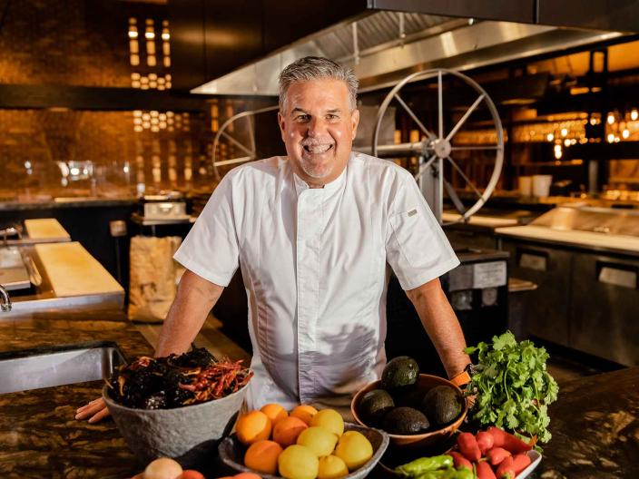 Richard Sandoval, head chef of Toro, in chef's attire with a collection of fruits and vegetables