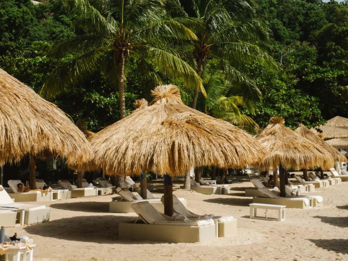 Beach recliners on Sugar Beach at the base of a mountain, each with thatched roof canopies