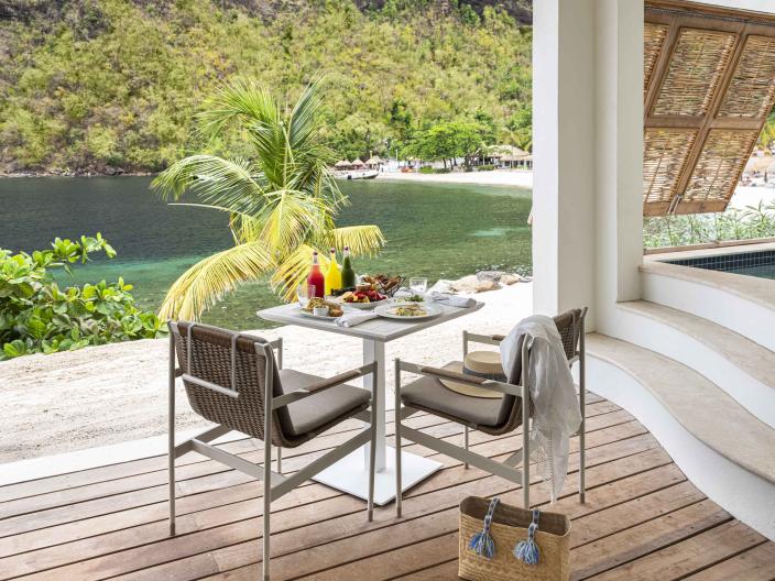 A patio table covered in food and drinks, next to a cove at Sugar Beach