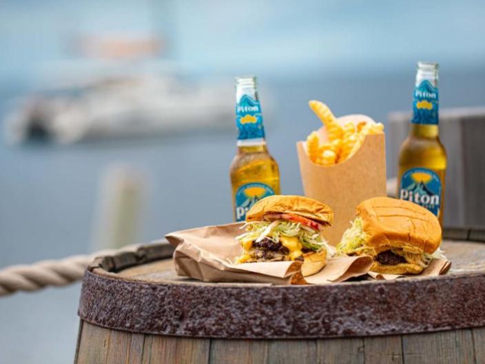 Two burgers, two beers and some french fries on a barrel with the ocean in the background