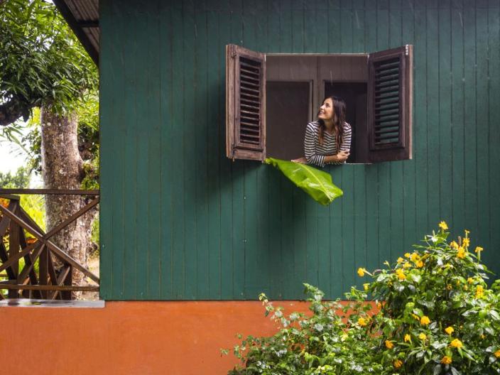A woman looks out the gabled window of a green residence at the tropical greenery surrounding her, at Viceroy Sugar Beach