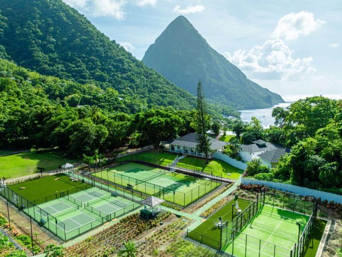 A trio of grass tennis courts, nestled amongst tropical trees at the base of the Pitons at Sugar Beach