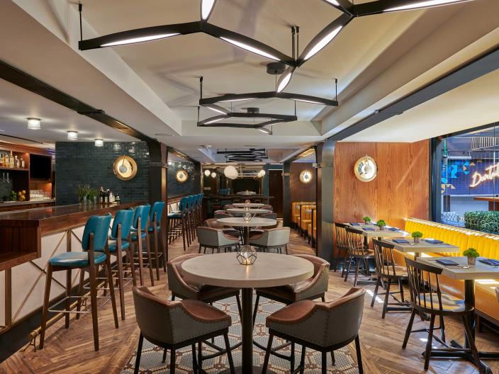 The dining room of Dovetail restaurant at Viceroy Washington DC, with a row of yellow booths adjacent to a long bar seating area