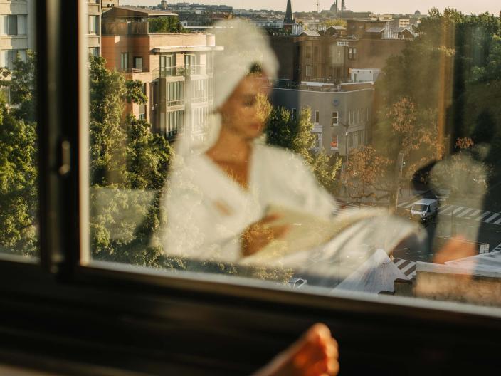 The reflection of a woman in a spa robe reading in a window