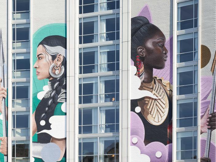 A mural of two women surrounded by neon colors, spanning five stories in height