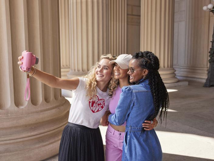 three woman take a selfie with a pink camera