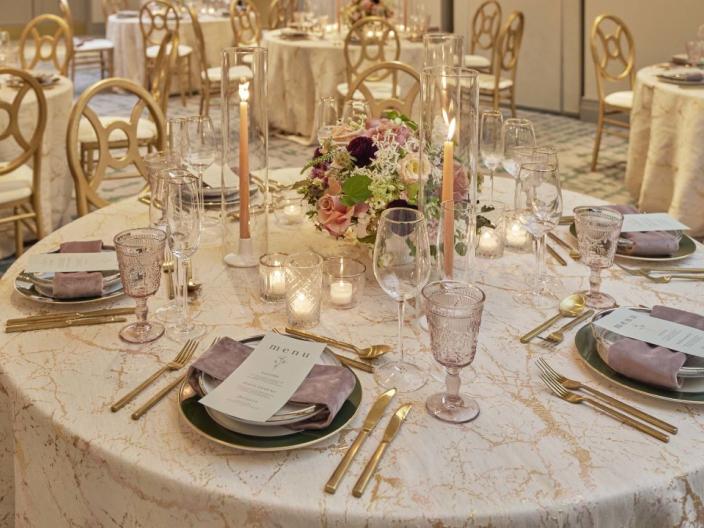 A banquet table decorated for a wedding at Viceroy Washington DC, with a white table cloth, tall candles and a flower centrepiece, and gold cutlery and finishe