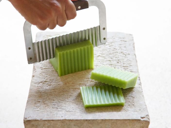 hand holding silver knife cuts green soap on table