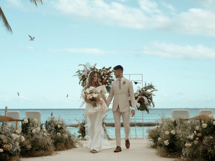 A newly married couple walk hand in hand back down the aisle, smiling at one another.