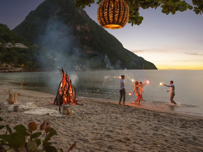 A family dances on the beach with sparklers at dusk. 