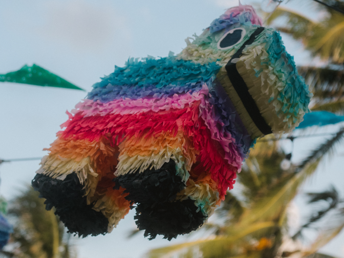 A colourful piñata swings in the air on the beach.
