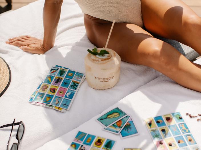 a woman on a towel with a mixed drink in a Viceroy coconut glass