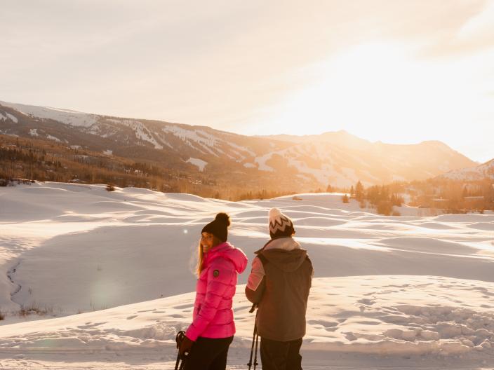 Two people skiing on the snow watching the sunset