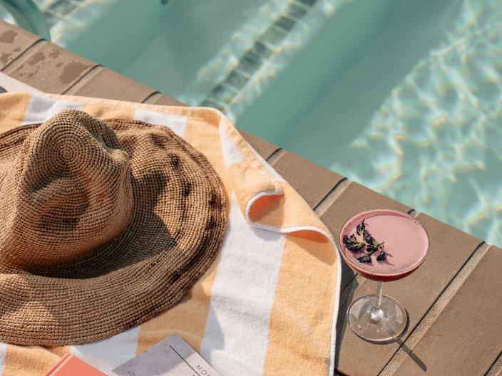 a poolside towel with books, a magazine, and cocktail