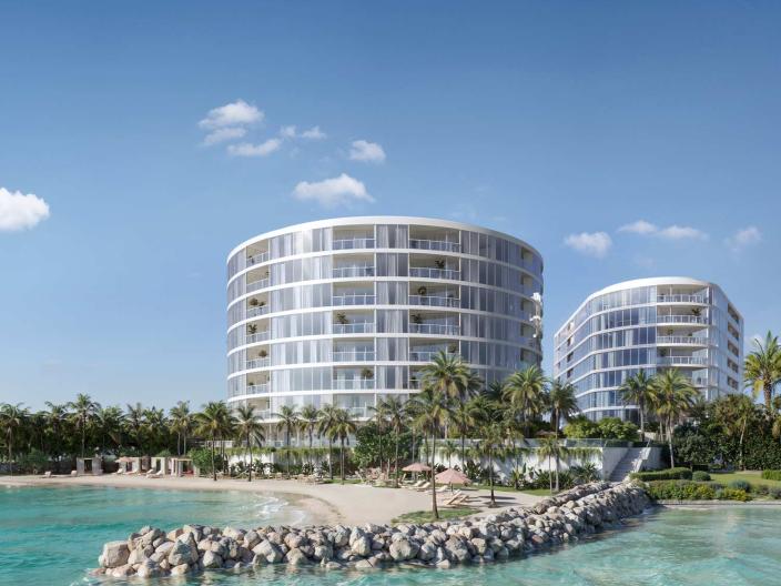 Par une journée ensoleillée, des immeubles d'appartements circulaires modernes se dressent derrière une plage bordée de palmiers et une jetée rocheuse.