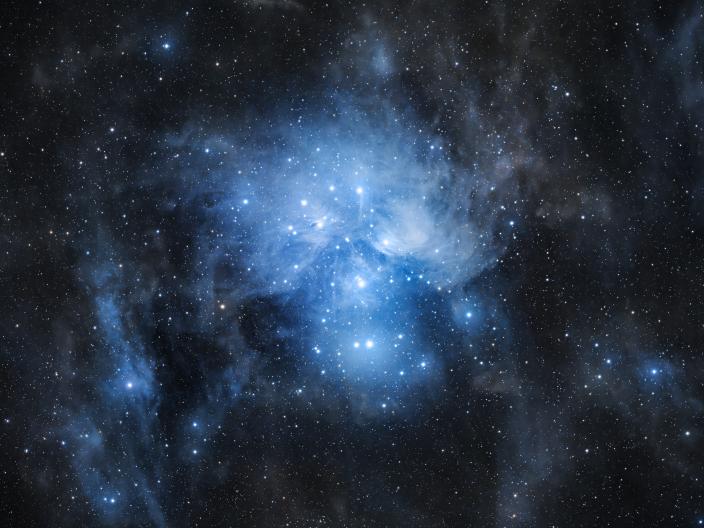 Um aglomerado estelar aberto e denso, conhecido como as Plêiades, brilha com uma nebulosa de reflexão azul bem distinta.