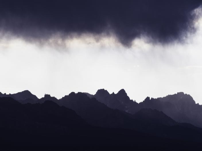 Cordilheira escarpada recortada contra uma nuvem de tempestade densa e escura, num céu pálido.