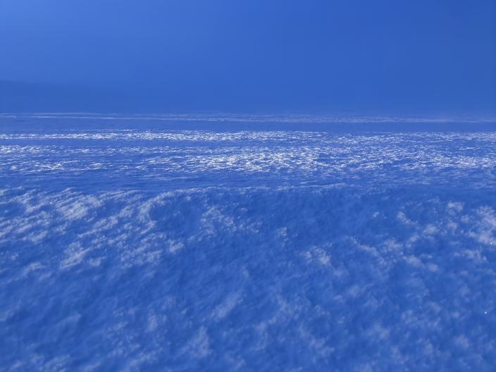 Um campo de neve de um azul profundo e texturado que se estende até um horizonte enevoado, sob um céu límpido.