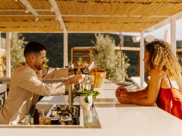 A bartender pours a drink for a woman sitting at an outdoor bar.