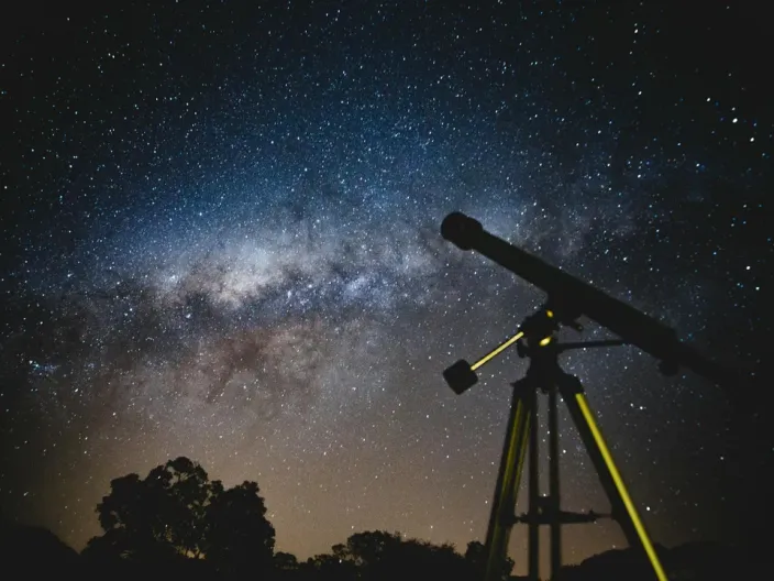 A telescope silhouetted against the starry expanse of the Milky Way.