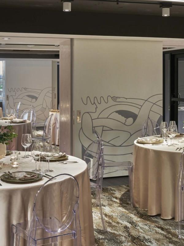Tables dressed in light-gold drapery and laid out in preparation for dining at an event.