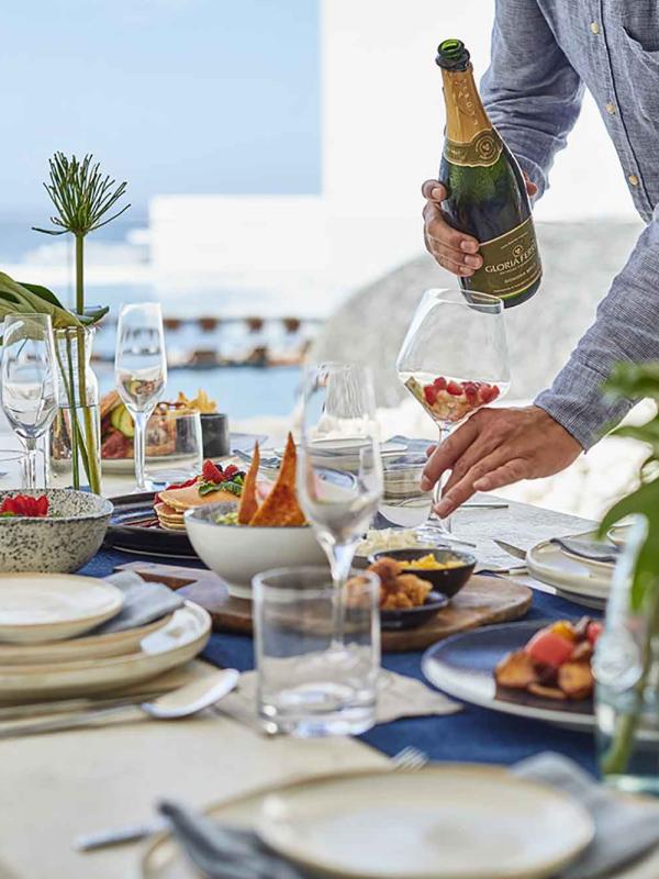 server pours a bottle of bubbly into a glass on a fully set table