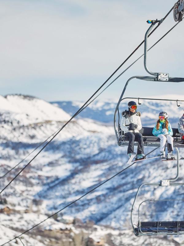 group of skiiers on chairlift with snowy mountains in background
