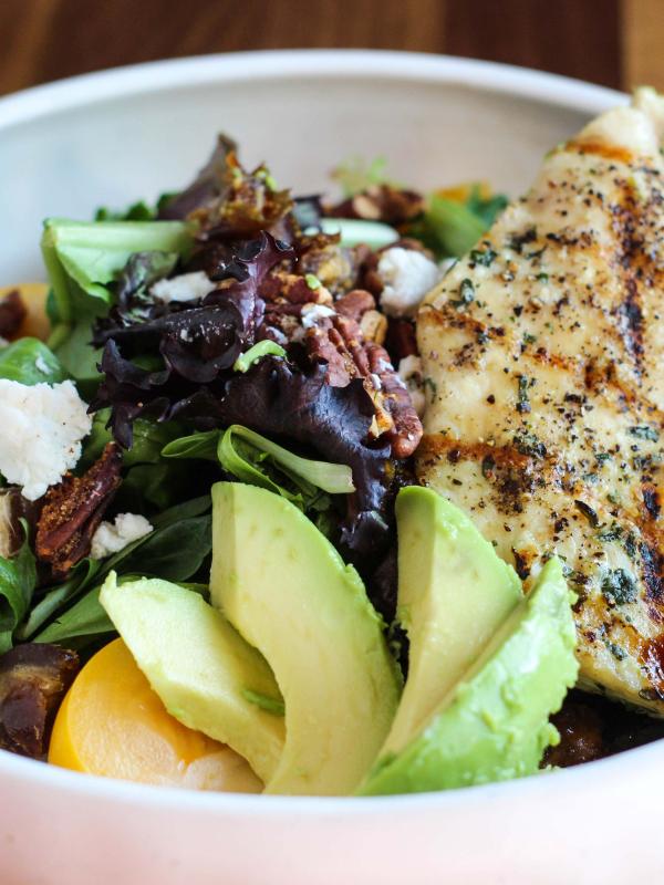 white bowl filled with greens, grilled chicken, and sliced avocado