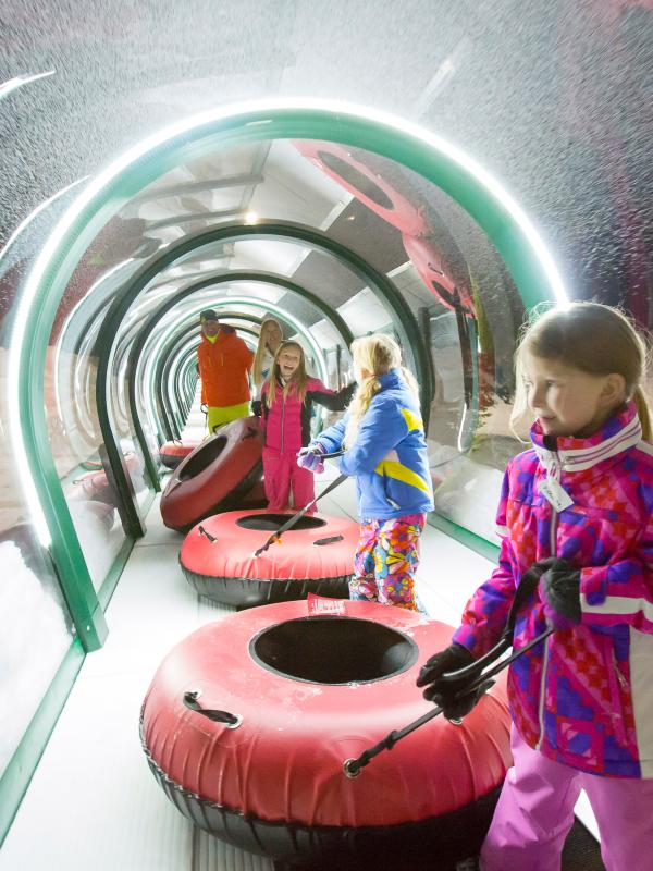 group of children holding tubes walk through an enclosed tube