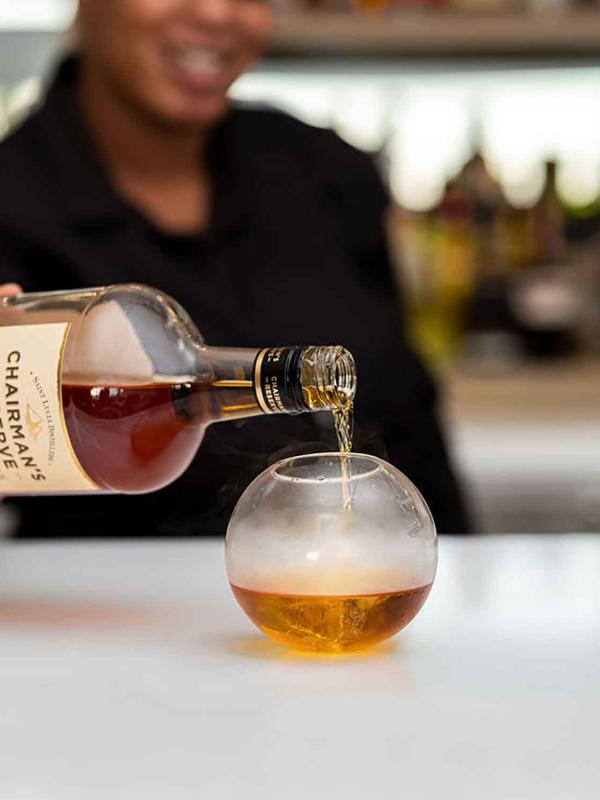 Bartender pouring rum into a spherical glass