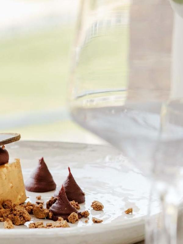A place setting of cake on the table, with vase, flowers, and wine glass containing water out of focus.