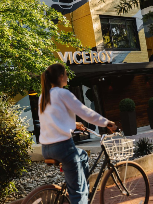 A woman rides a bicycle past the facade of Viceroy Chicago