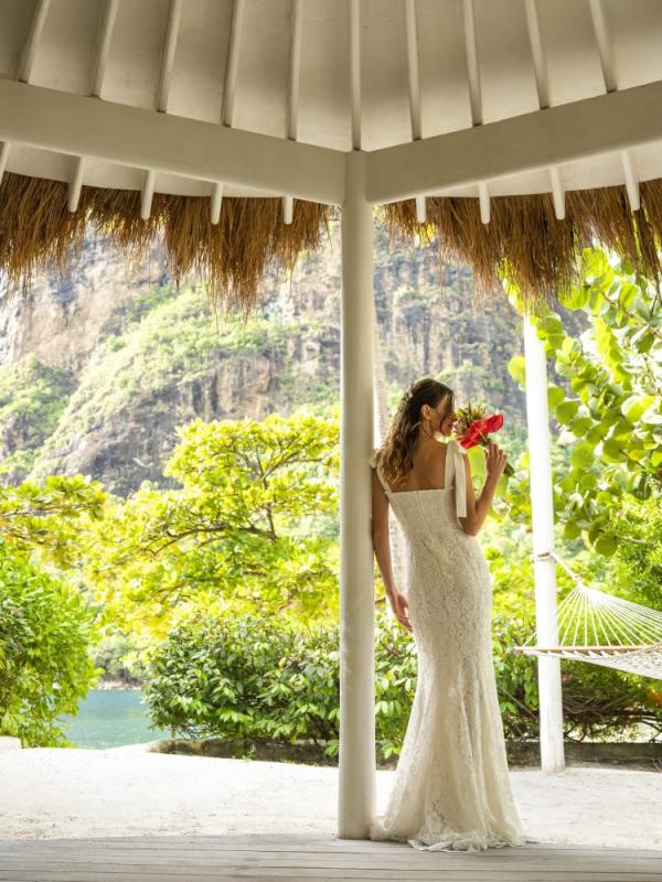 A bride smells her bouquet in a courtyard, next to a hammock looking out on a tropical landscape