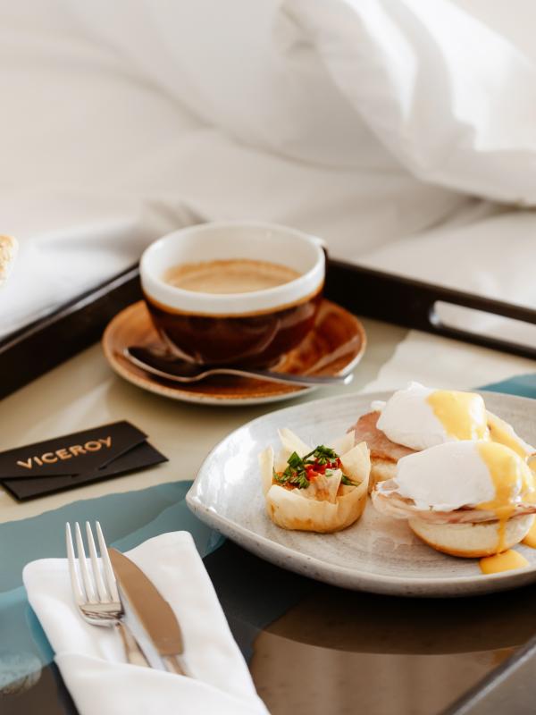 Una bandeja de desayuno en la cama, con un sándwich de huevo y un café