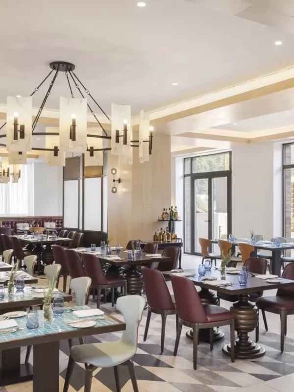 The Mountain Kitchen at Viceroy Kopaonik Serbia, a large bright room with a long row of benches and tables with high-back chairs, under a large chandelier