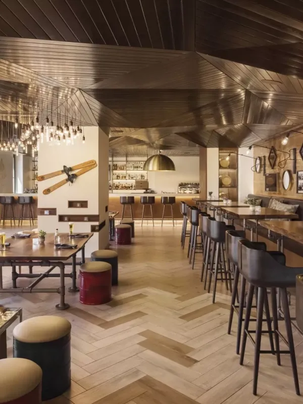 The dining room of Pique Ski Bar, with a long bar, several tables and ski paraphenalia decorating the ceiling