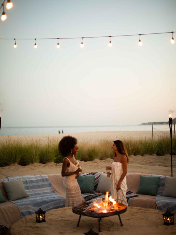 Two women at an outdoor fie pit near the Las Cabos beach having a conversation