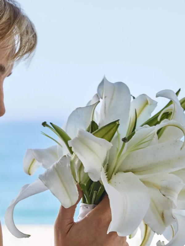 A woman in a white dress smiling while staring flowers she is holding while at Viceroy Los Cabos