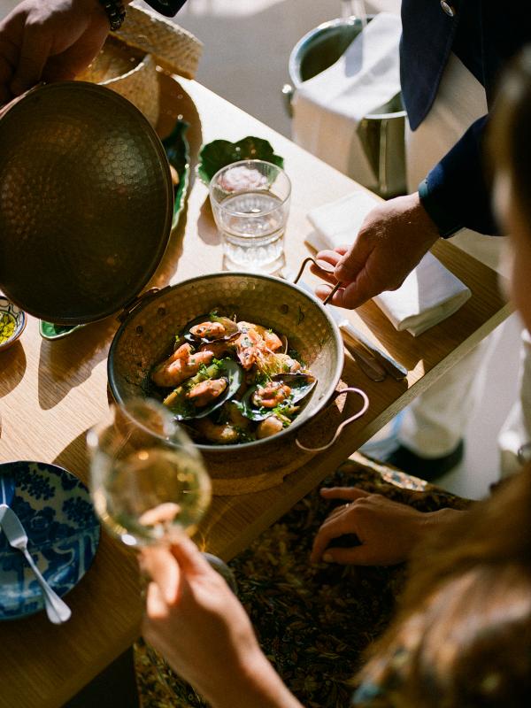 A server places a seafood dish in front of a diner who is enjoying a glass of wine