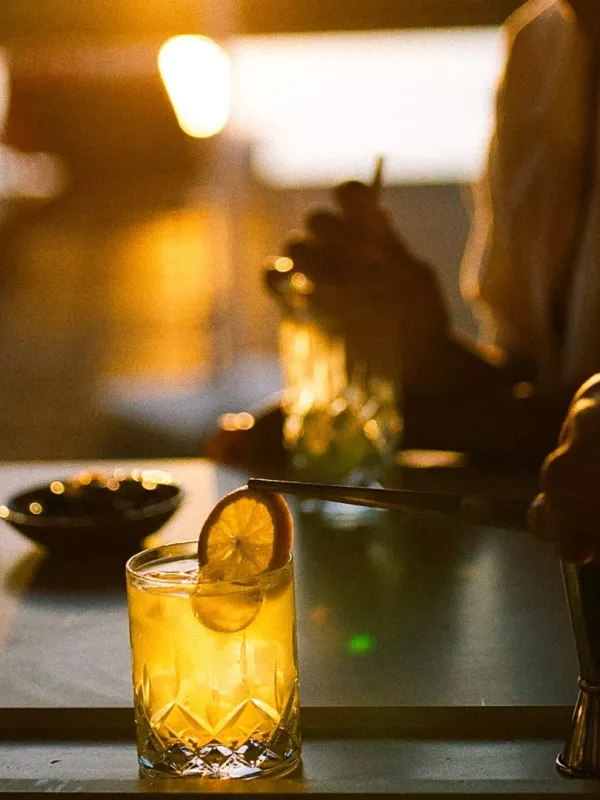 Patrons around a table at Salpico Pool Bar enjoy a bright orange drink with an orange garnish, at dusk