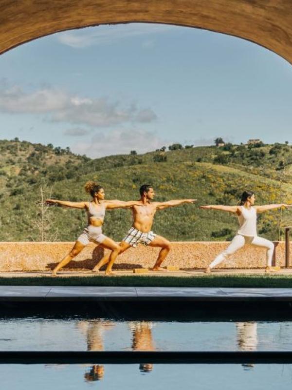 Three people doing yoga in a spa courtyard at Viceroy Ombria Algarve, with rolling hills in the background