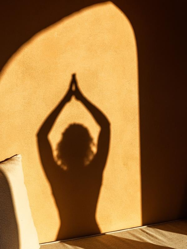 The shadow of a person doing a yoga pose on a stone wall