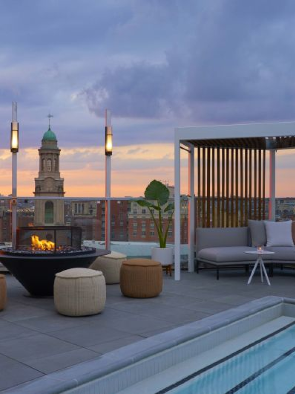 A rooftop patio with a bankette couch, ottomans and torch lighting