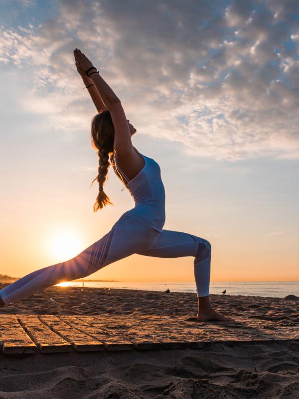 A woman does yoga on Santa Monica beach at sunset