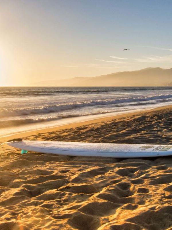 A surfboard lying on a Santa Monica beach at sunset
